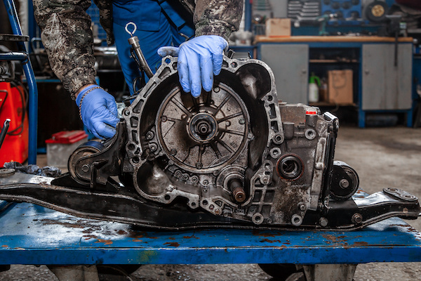 A close-up of a young man repairman in a working uniform of cars is repairing an automatic gearbox of a used car in an auto repair shop. The concept of car repair and car repair shop